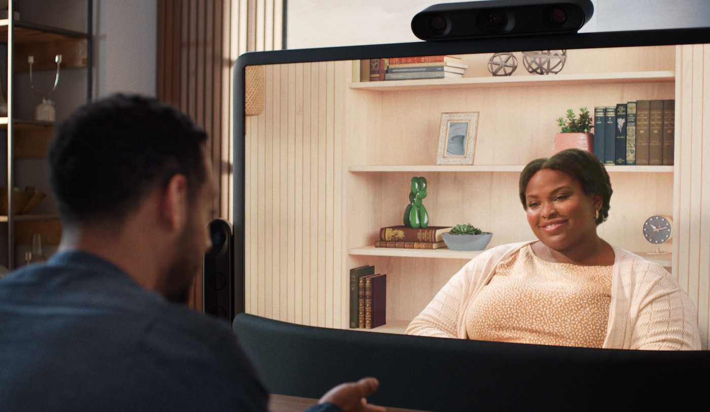 Person seated at laptop in office stands up and checks smartphone screen. Person seated on bench with headphones on looks at laptop screen with hands clasped. Person seated at desk alone in office types on laptop. Two people talk and smile at conference table with laptops open. Two people using American sign language have a conversation seated on the same side of an office table. One person signs “That’s not a good idea”. Close up of person’s face while signing. Person smiling in response. Close up on seated person talking to another person in a seat. They gesture in conversation. Camera moves back to reveal the Starline display and table and that they are using Starline for their conversation. We see both individuals on the Starline display gesturing and smiling in conversation. 