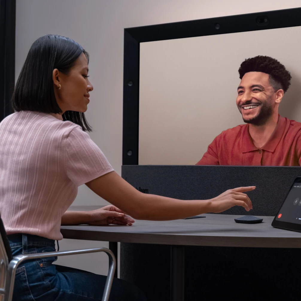 A person is smiling from a Beam display. The person on the other side of the Beam display is visible.